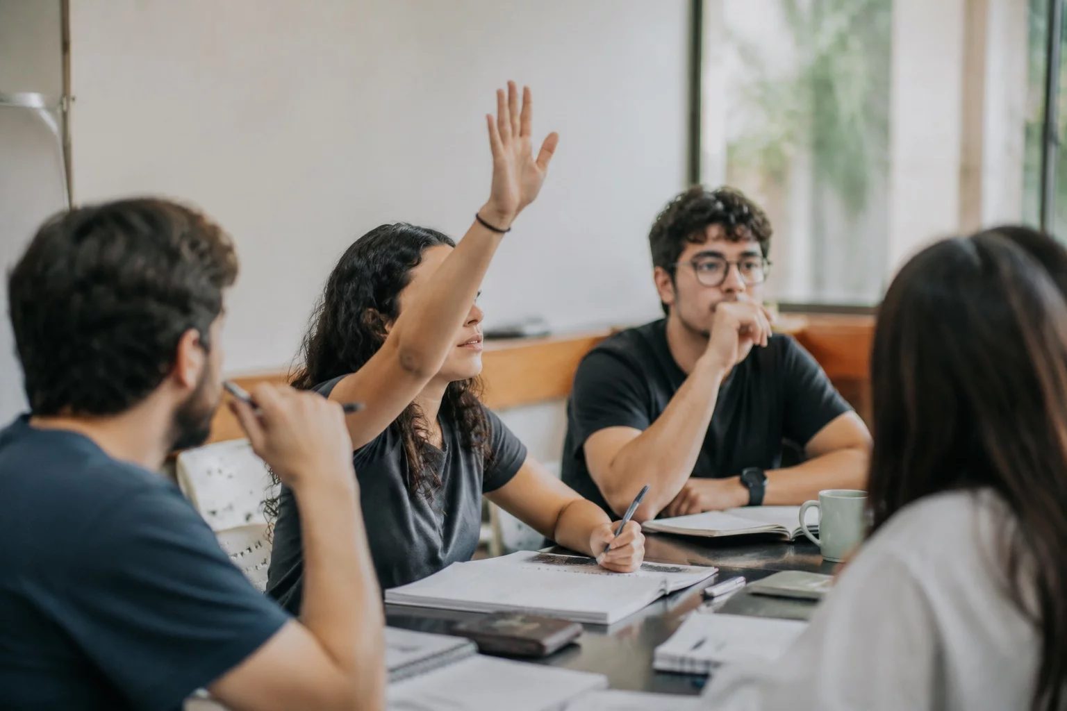 Estudante levantando a mão em uma mesa de seminário coberta de anotações