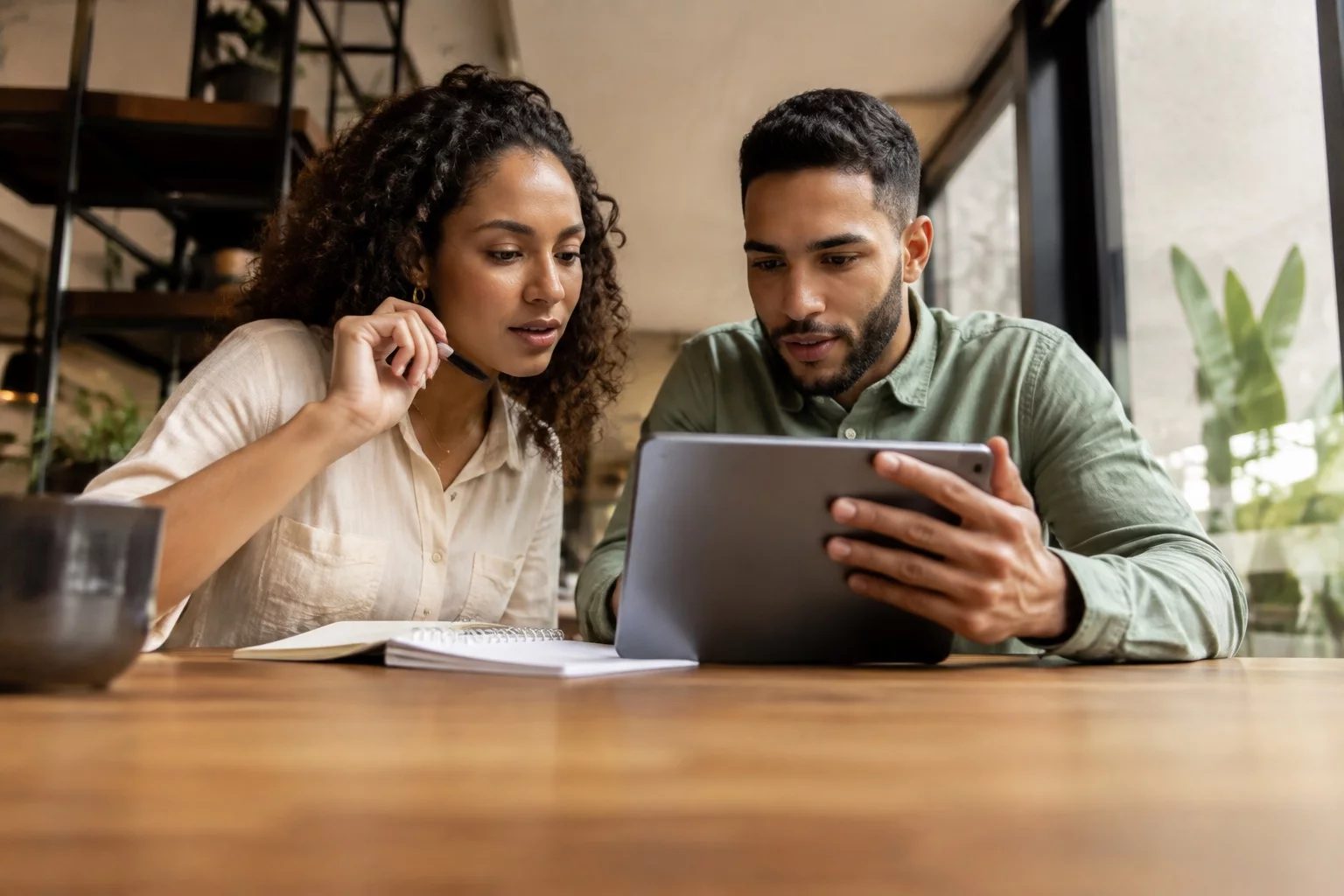 Duas pessoas revisando anotações em um tablet sobre uma mesa de madeira